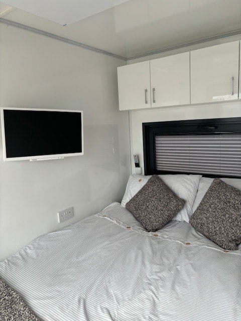 Bedroom with wall-mounted TV, overhead storage and striped bedding