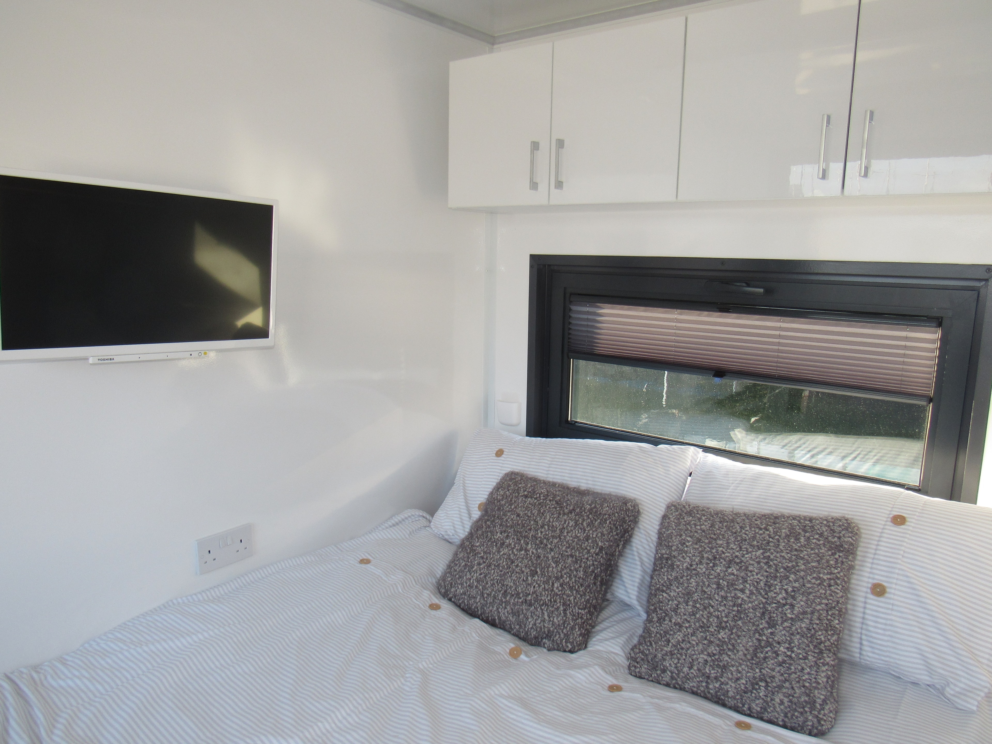 Bright bedroom with wall-mounted TV, overhead storage and marina window