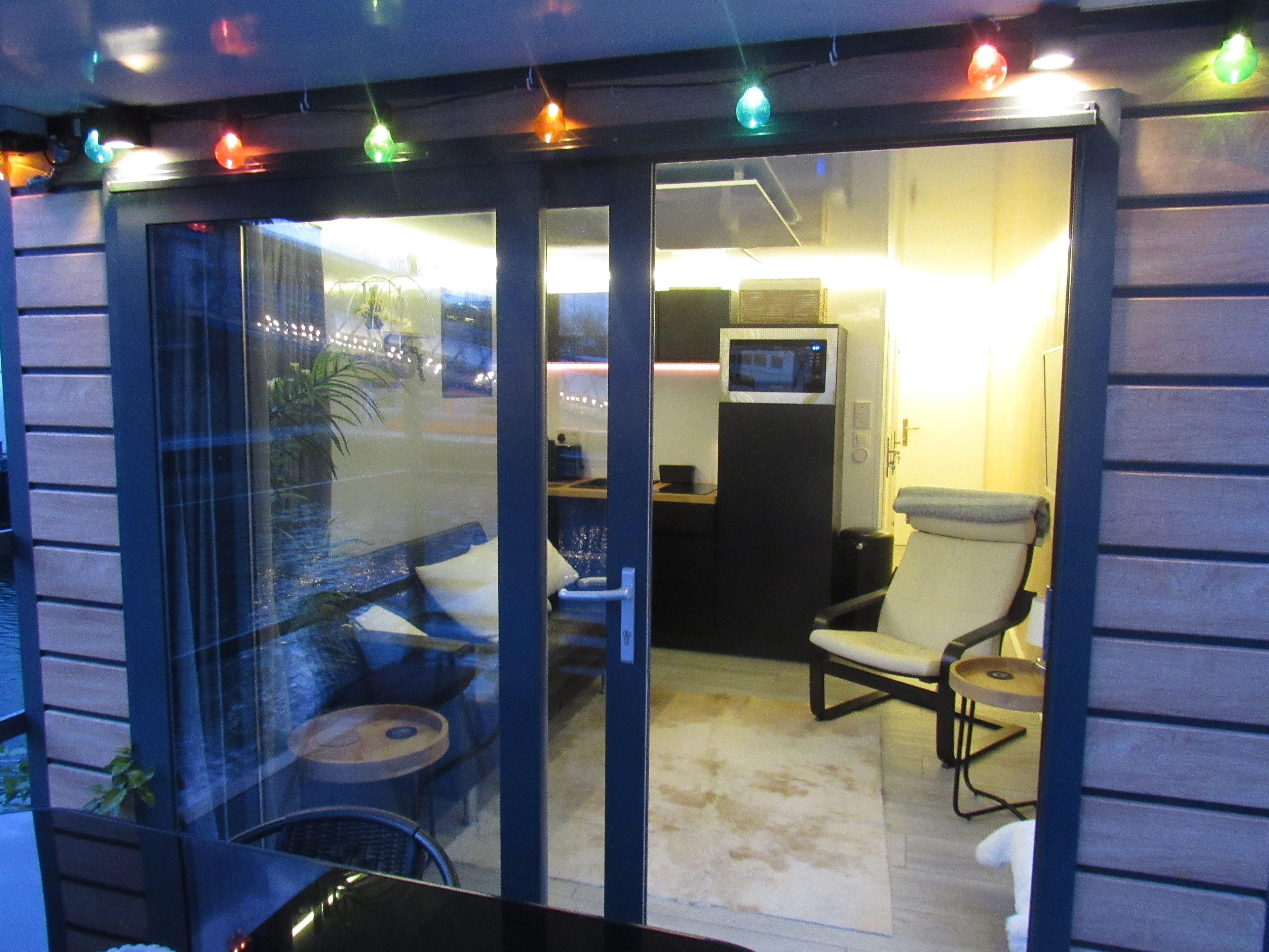 Evening view through the glass doors showing the lit interior and coloured fairy lights