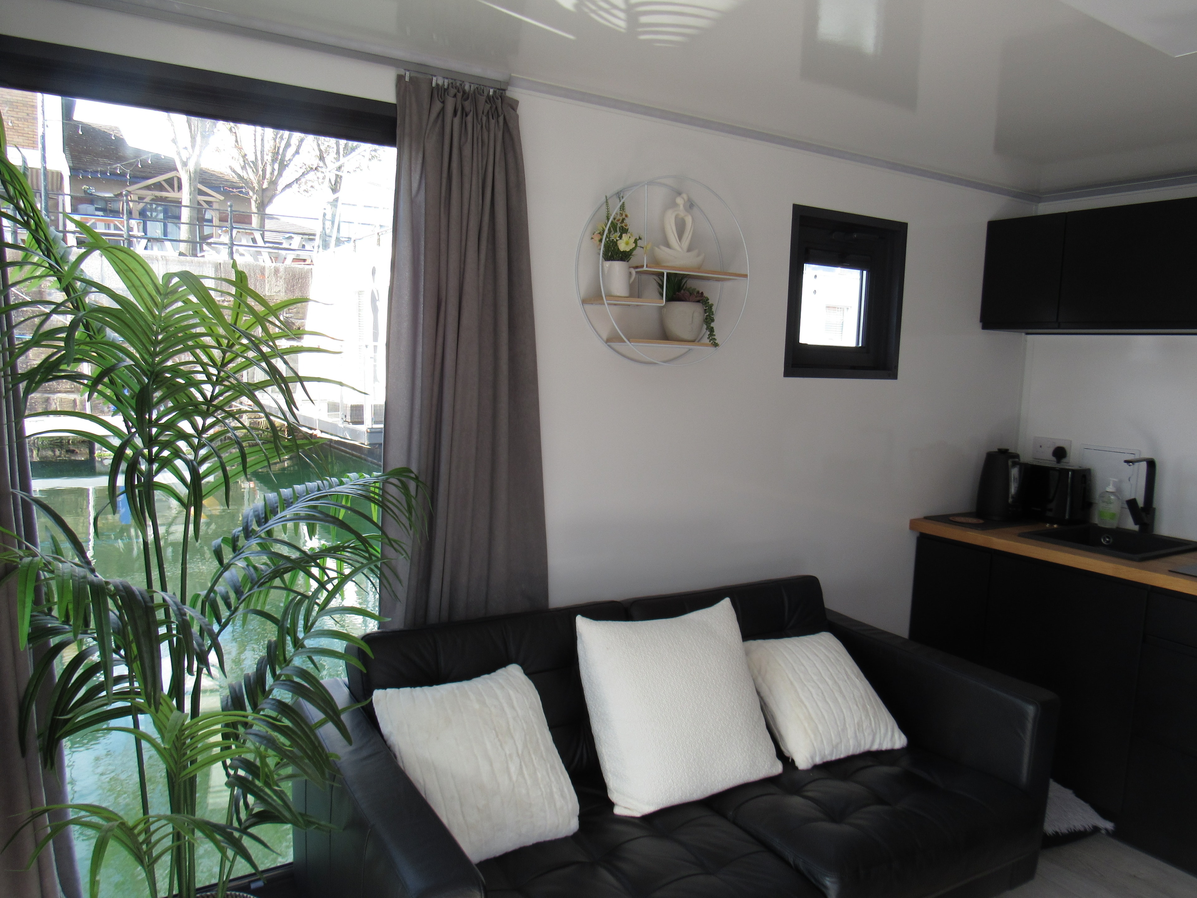 Black leather sofa with white cushions and large palm plant beside the canal-view window