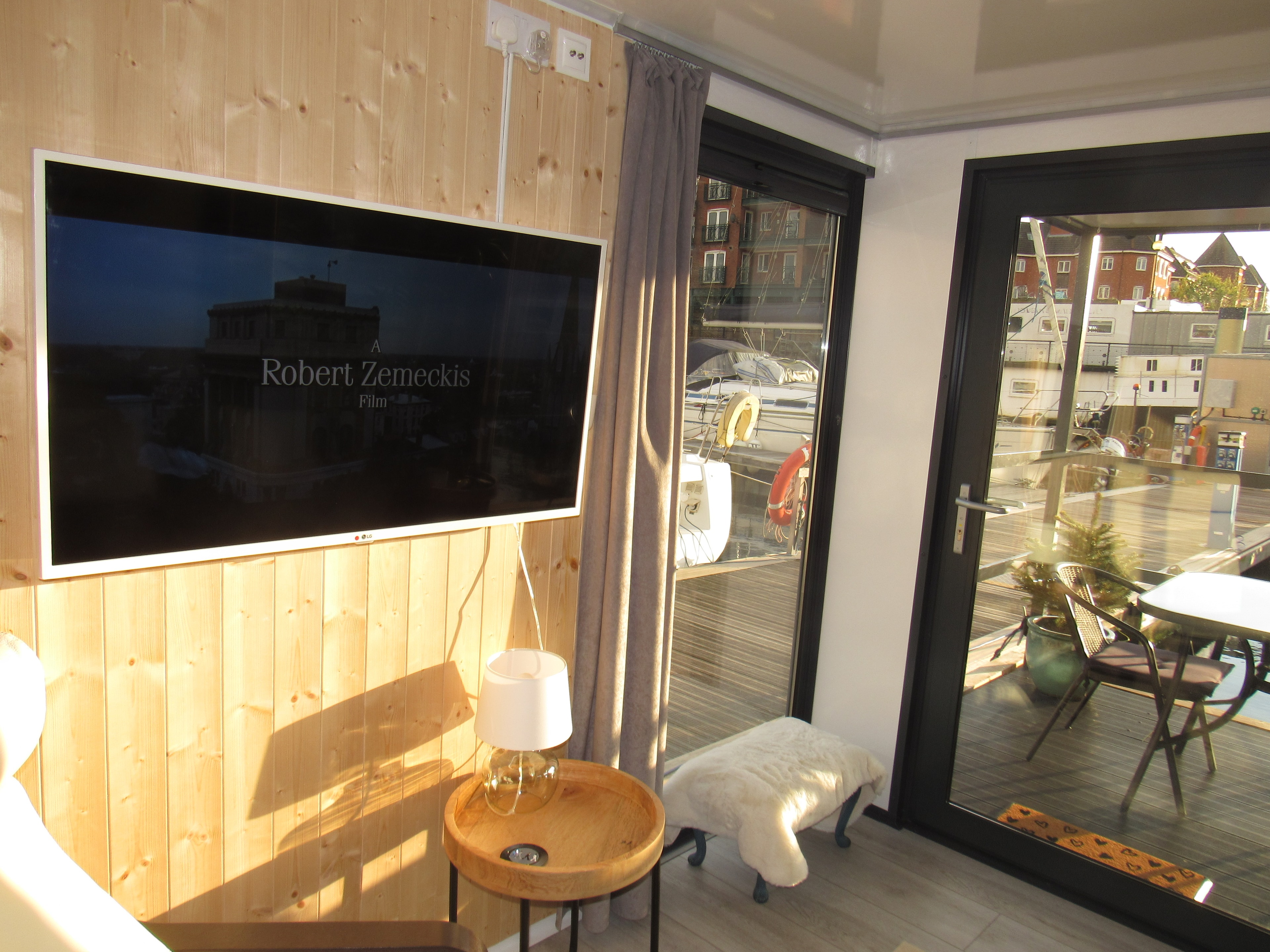 Sunlit TV wall with round side table and glass doors open to the balcony and marina